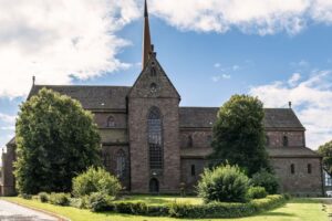 Historische Kirche mit hohem Turm und gepflegtem Garten unter blauem Himmel